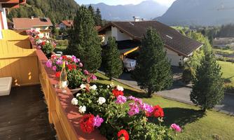A beautiful balcony with colorful flowers and a view of the mountains. In the background, there are small houses and green trees.