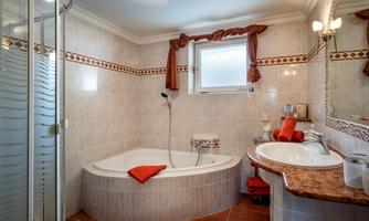 A modern bathroom with a bathtub and a separate shower. There are bright tiles, a large mirror, and decorative towels.