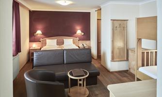 A cozy hotel room with a double bed and a seating area. The warm colors and the wooden details create an inviting atmosphere.