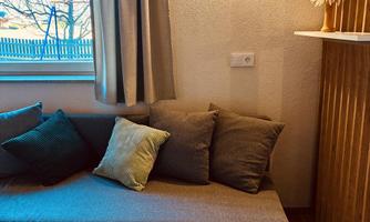A cozy corner with a gray sofa and colorful cushions. The room has a warm light and a modern touch.