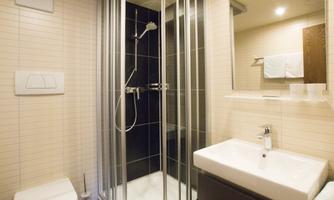 A modern bathroom with a shower and a sink. The walls are tiled in light colors and there are towels nearby.