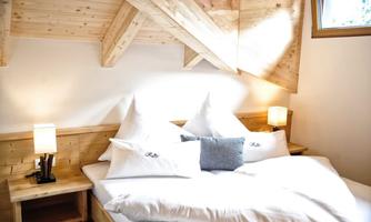 A cozy bedroom with a wooden bed and two nightstands. The walls are made of wood and there is soft lighting.