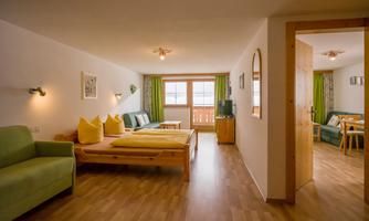 A bright, modern apartment with wooden floors and large windows. It is furnished with comfortable sofas, a table, and colorful cushions.
