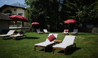 A relaxed sunbathing lawn with loungers and red sun umbrellas, surrounded by trees. The area invites you to relax outdoors.