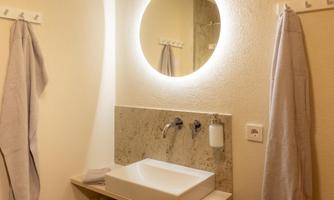 A modern bathroom with a sink and a round illuminated mirror.