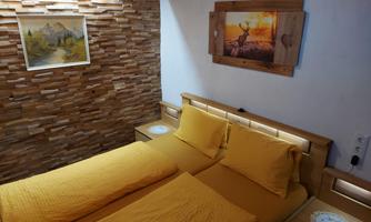 A cozy room with a double bed and yellow bedding. The walls are decorated with wooden panels and there are artworks on the walls.