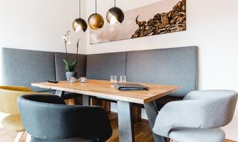 A modern dining room with a wooden table and comfortable chairs. Stylish lamps hang above the table, and a pictorial motif can be seen on the wall.