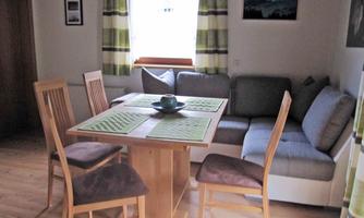 A cozy dining area with a table and four chairs. The windows are decorated with striped curtains, and a couch is positioned against the wall.