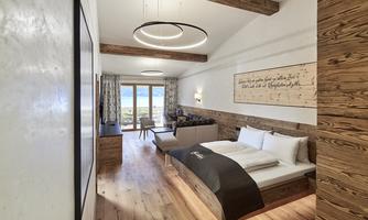 A modern hotel room with wooden elements and large windows. The space is bright and inviting, with a view of the landscape.
