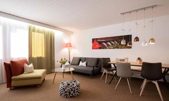 A modern living room with a cozy seating area and a dining space. Large windows provide plenty of daylight and a welcoming atmosphere.
