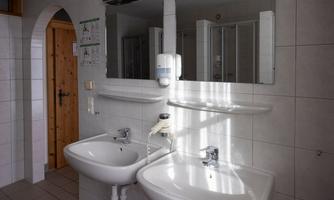 A modern bathroom with two sinks and mirrors. In the background, a shower and wooden paneling are visible.
