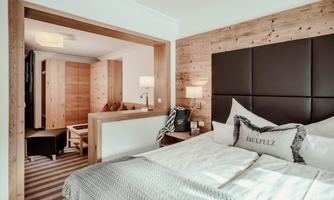A modern bedroom with wooden elements and a large bed. The room has a cozy atmosphere and a separate living area.