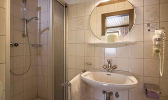 A modern bathroom with a shower, a washbasin, and a round mirror. The walls are tiled and the ambiance is clean and inviting.