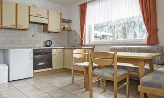 A bright kitchen with wooden furniture and a dining table. The room has large windows that offer a view of the landscape.