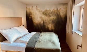 A cozy bedroom with a large bed and soft pillows. The wall is decorated with a natural motif of a forest landscape. View of the surrounding mountainous scenery.
