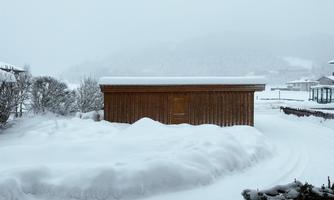 A wooden shed stands amidst deep snow. The landscape is covered by a thick layer of snow, and visibility is limited.