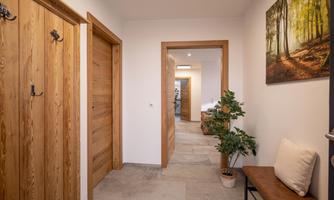A modern hallway with wooden doors and a bench. A picture of a forest hangs on the wall, and a plant stands next to the bench.