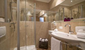 A modern bathroom with a shower and a sink. The walls are tiled in light colors and there is a large mirror.