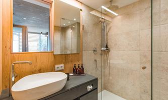 A modern bathroom with a large shower cabin and an elegant sink. The walls are designed with bright tiles and wooden paneling.