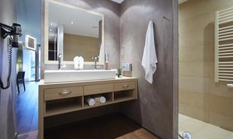 A modern bathroom with a large sink and a mirror. The decor is simple and elegant, featuring light wood and neutral colors.