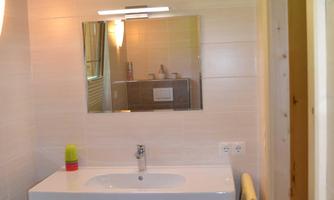 A modern bathroom with a large mirror and a stylish sink. The walls are light and the floors are made of dark tiles.