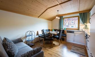A cozy living kitchen with a dining area and a sofa. Bright walls and wooden ceilings create a friendly atmosphere.