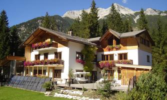 A beautiful holiday home surrounded by trees and mountains. The garden is well-maintained and the balconies are decorated with flowers.