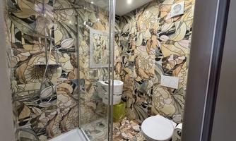 A modern bathroom with a glass shower and colorful, floral tiles. The fixtures include a sink and a toilet.