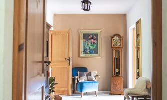 A cozy living room with a blue armchair and a beautiful carpet design. Bright walls and wooden details create an inviting atmosphere.