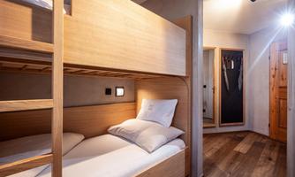 A cozy bedroom with a bunk bed made of light wood. The walls are neutral, and the room is well-lit.