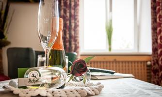 An elegant table decoration with a champagne bottle, glasses, and a rose. The room has a cozy ambiance with a window in the background.