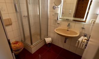 A small bathroom with a shower and a sink. The walls are tiled and the furnishings are functional.