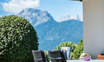 An inviting outdoor area with a table and chairs. In the background, mountains and a blue sky can be seen.