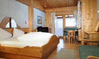 A cozy room with wooden decor and a large bed. There is a workspace and a balcony with a view outside.