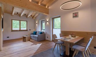 A modern living room with a wooden ceiling and large windows. There is a cozy couch and a dining table with chairs.
