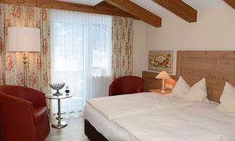 A cozy bedroom with a double bed and two red armchairs. The walls are decorated with floral curtains and a window lets in plenty of natural light.