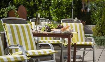 A cozy terrace with striped chairs and a table. The table is set with wine, grapes, and fresh bread.