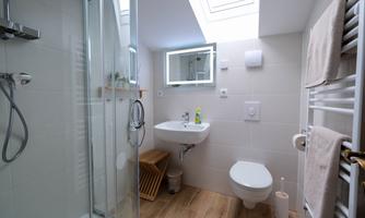 A modern bathroom with a large shower, a sink, and a toilet. It has bright tiles and a skylight that lets natural light shine in.