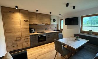 A modern kitchen with wooden cabinets and a dining table. It features a cooking area, an oven, and a cozy seating area.