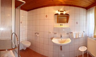 A modern bathroom with a shower area, a sink, and a toilet. The walls are decorated with white tiles and wood paneling.