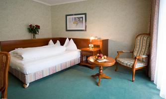 A cozy hotel room with a bed and a comfortable armchair. Fresh fruit is on the table and there is a beautiful decoration on the wall.