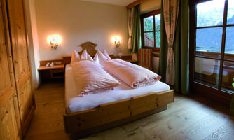 A cozy bedroom with a double bed and large windows. The room is decorated with wooden furniture and warm lighting.