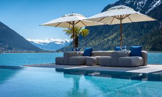 A beautiful pool area with sun loungers and umbrellas. In the background, majestic mountains extend under a clear blue sky.