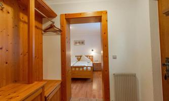 A bright hallway with wooden shelves and a view of a bedroom in the background. The walls are neutral, and the floor is made of wood.