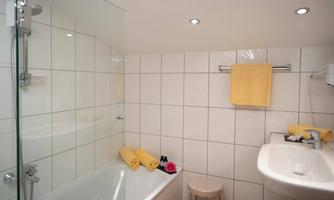 A modern bathroom with a shower and a bathtub. There are yellow towels and a small wooden stool.