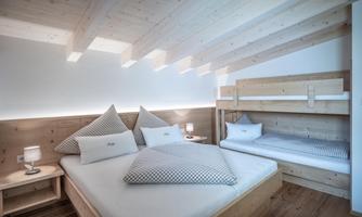 A modern bedroom with wooden paneling and sloped ceilings. There is a large bed and a bunk bed, ideal for families.