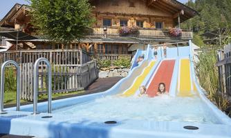 A water park with colorful slides and happy children playing in the water. In the background, a beautiful traditional wooden house can be seen.