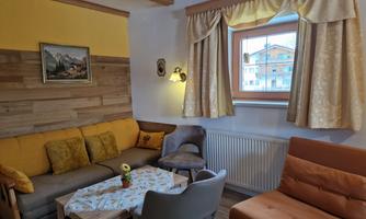 A cozy room with a beige couch and an orange armchair. The window lets in plenty of daylight and shows the outside view of the house.