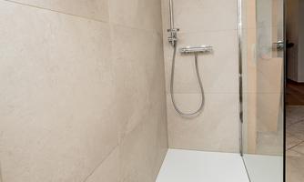 A modern tiled shower with clean lines and glass partition. Towels and a gray bath mat are ready.