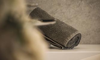 A gray towel is lying on a white shelf. In the background, a simple, modern wall can be seen.